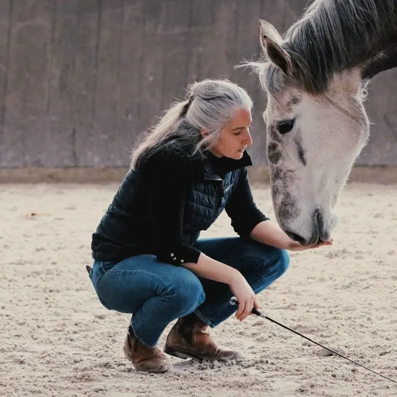 Léa Forge compartilha um momento de cumplicidade e confiança com um cavalo cinzento durante uma sessão de equitação etológica no picadeiro.