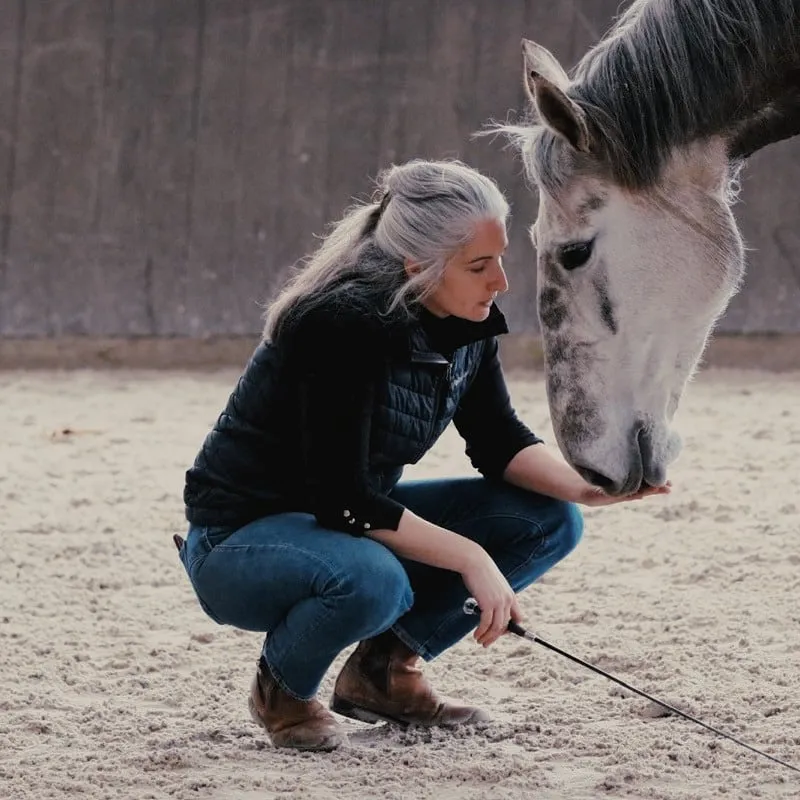 Léa, agachada, estende a mão para seu cavalo